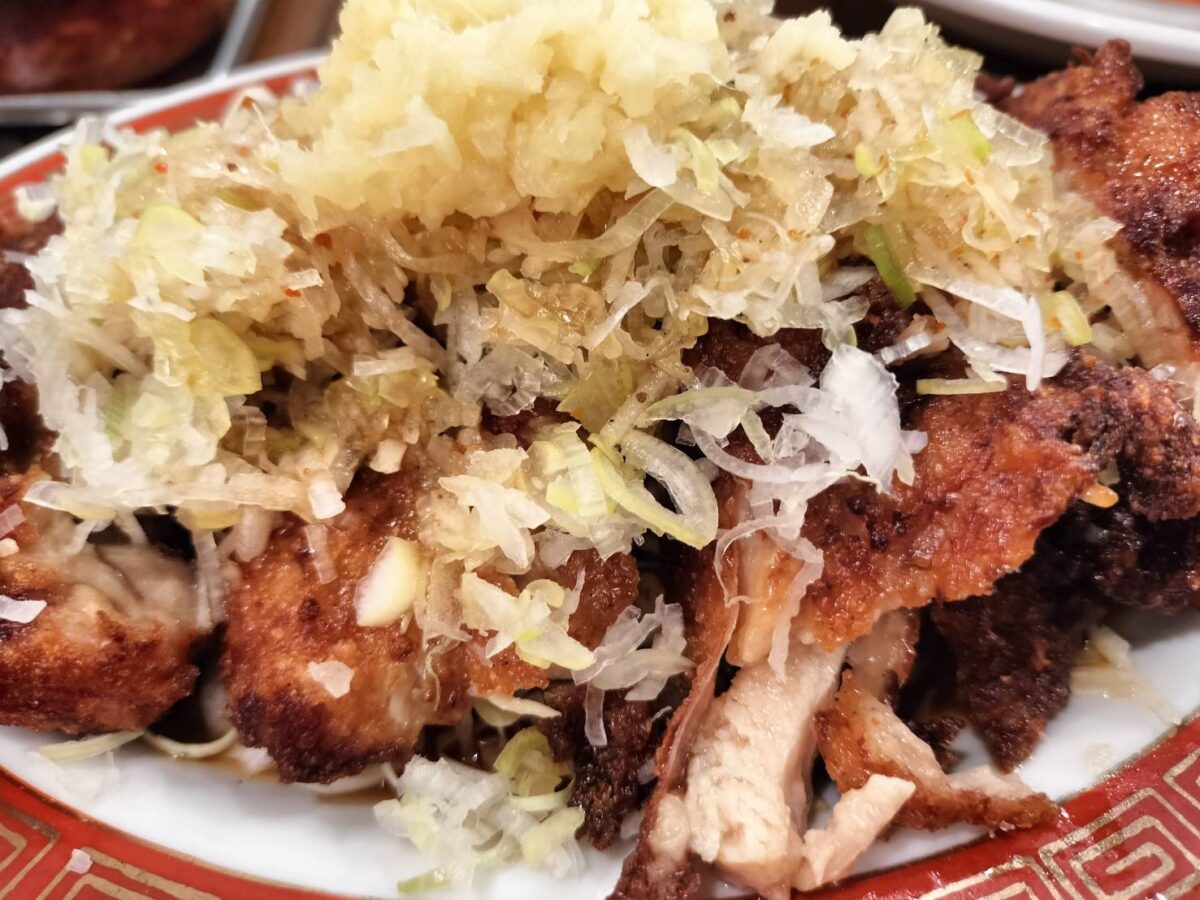 広州市場の油淋鶏。カリカリに揚げた鶏肉の上に、キャベツと生姜、ネギなどの薬味が山盛りに乗っている様子。